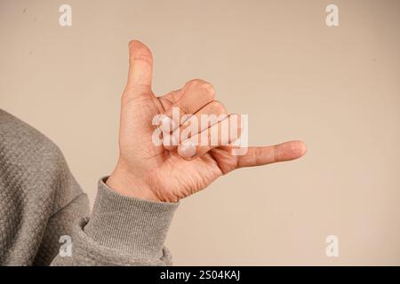 Une main montre un geste avec trois doigts pressés contre la paume (index, milieu et anneau), tandis que le pouce et le pinky sont étendus Banque D'Images