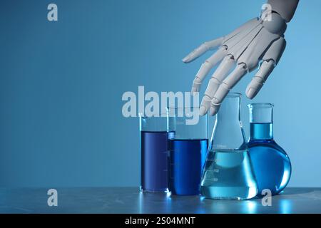 Intelligence artificielle. Main de robot et verrerie de laboratoire avec des liquides sur la table sur fond bleu clair, espace pour le texte Banque D'Images