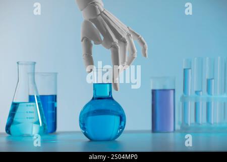 Intelligence artificielle. Main de robot avec flacon et autre verrerie de laboratoire avec des liquides sur la table sur fond bleu clair Banque D'Images