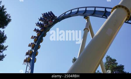 Les gens traversent une inversion sur les montagnes russes inversées intenses 'Ozlris' du fabricant 'B&M' dans le parc à thème 'Astérix' sous un SK bleu Banque D'Images