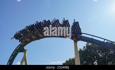 Les gens traversent une inversion sur les montagnes russes inversées intenses 'Ozlris' du fabricant 'B&M' dans le parc à thème 'Astérix' sous un SK bleu Banque D'Images