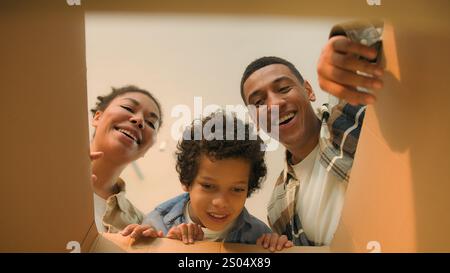 Point de vue POV boîte ouverte afro-américaine famille parents fils déballage colis en carton heureux drôle petit garçon enfant enfant surprise ours en peluche jouet Banque D'Images