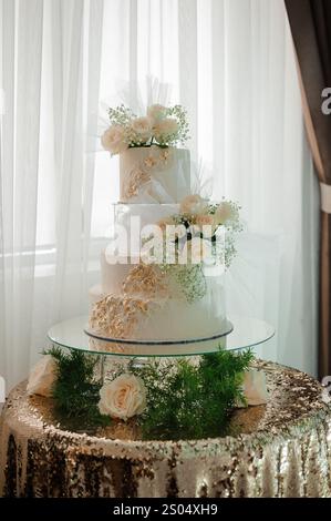 Elégant gâteau de mariage blanc orné de fleurs fraîches et d'accents dorés. Banque D'Images