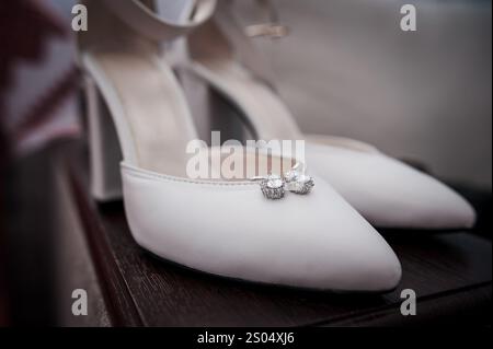 Talons hauts blancs élégants avec accessoires étincelants sur une surface en bois. Banque D'Images