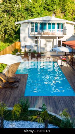 Arrière-cour moderne avec piscine, terrasse en bois et verdure luxuriante entourant une élégante maison de deux étages Banque D'Images