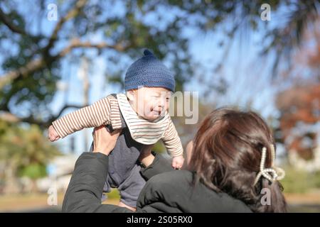 Par un froid après-midi d'hiver dans un parc à Hakata, préfecture de Fukuoka, une femme de 30 ans portant une veste en duvet et un bébé japonais de 5 mois sourient as Banque D'Images