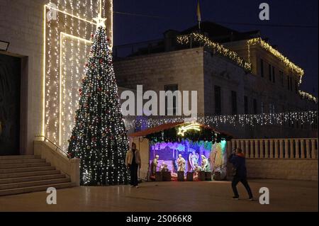 Les gens posent pour des photos à côté d'une crèche de scène de la nativité représentant la naissance de Jésus et un arbre de Noël décoré exposé à l'extérieur de l'église catholique romaine Joseph administrée par l'ordre des Carmélites, située dans la colonie allemande le 24 décembre 2024 à Haïfa, Israël. Banque D'Images