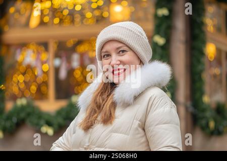 Femme souriante de 30-35 ans sur fond de lumières colorées de guirlandes pendant les vacances festives dans l'une des villes. Banque D'Images