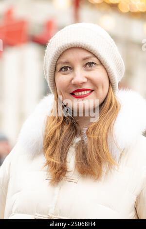 Femme souriante de 30-35 ans sur fond de lumières colorées de guirlandes pendant les vacances festives dans l'une des villes. Banque D'Images