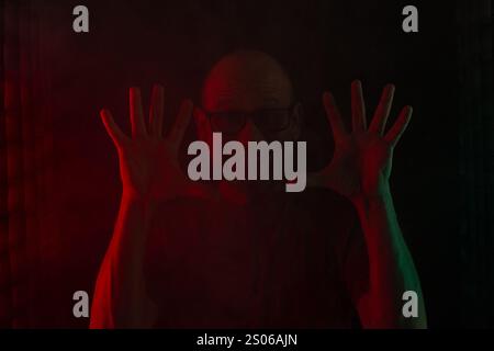 Homme chauve et barbu avec des lunettes de vue souriant et montrant les doigts des deux mains à la caméra. Isolé sur fond rougeâtre foncé. South AME Banque D'Images