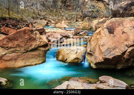 Un courant d'eau coule entre de grosses roches. L'eau est d'une couleur bleu vif. Les roches sont brunes et rugueuses. La scène est paisible et sereine Banque D'Images