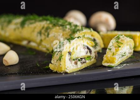 rouleau de pommes de terre cuit au four avec garniture de fromage cottage à l'ail et aux champignons, isolé sur fond noir. Banque D'Images