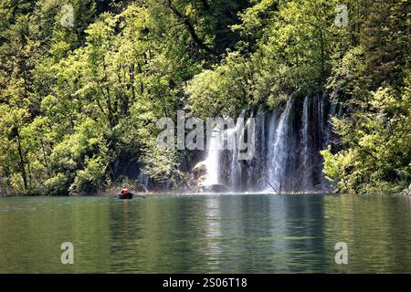 Un visiteur profite de la beauté d'une cascade encadrée par une végétation luxuriante dans le parc national des lacs de Plitvice, en Croatie, où la tranquillité de la nature est Banque D'Images