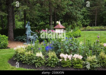 Lifesize statue de chasseur avec ses chiens à côté de la frontière avec des fleurs blanches Astilbe dans le jardin de campagne de la cour avant en été, le jardin de François jardin. Banque D'Images