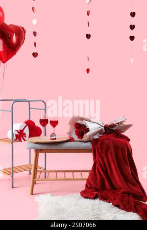 Banc gris avec des verres de vin, des roses et des décorations pour la célébration de la Saint-Valentin sur fond rose Banque D'Images