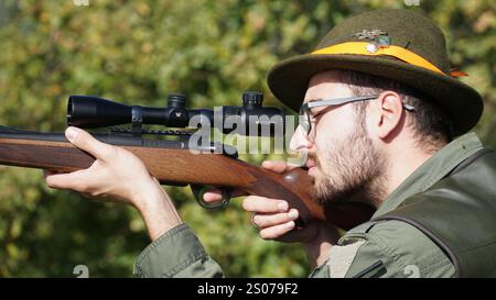 Hunter en camouflage vise son fusil dans une forêt dense, se mélangeant avec l'environnement naturel. L'image capture un lien entre l'homme et la nature. Banque D'Images