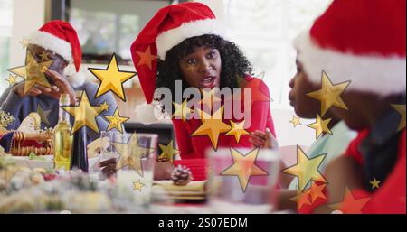 Image de stars sur une famille afro-américaine avec des chapeaux de père noël ayant le dîner de noël Banque D'Images