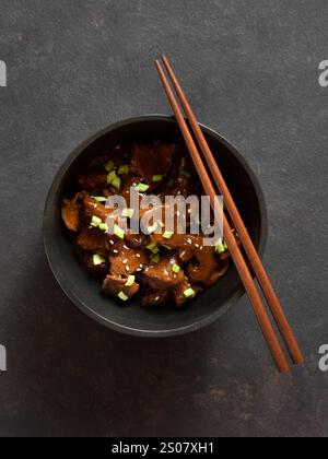 Boeuf avec sauce soja, oignon vert et graines de sésame dans un bol sur fond de pierre sombre. Vue de dessus, pose à plat Banque D'Images