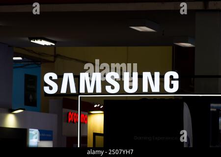 Signe lumineux blanc du logo de la marque Samsung brillant sur un fond sombre dans un magasin intérieur ou un cadre d'exposition. Banque D'Images