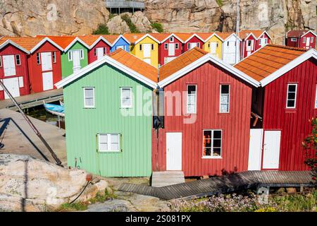 Des cabanes à bateaux en bois colorés alignés contre la falaise rocheuse le long du canal marin dans le vieux port de pêche de Smögen, en Suède, par une journée d'été ensoleillée. Banque D'Images