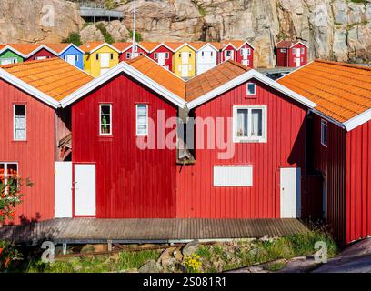 Des cabanes à bateaux en bois colorés alignés contre la falaise rocheuse le long du canal marin dans le vieux port de pêche de Smögen, en Suède, par une journée d'été ensoleillée. Banque D'Images