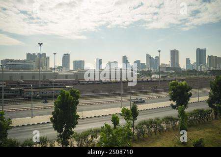 Bangkok, Thaïlande. 24 décembre 2024. Une vue sur le paysage urbain de Bangkok, avec une cour de chemin de fer avec plusieurs voies ferrées, une route à circulation clairsemée d'arbres, et en arrière-plan, le centre-ville de Bangkok avec des gratte-ciel, par une journée nuageuse avec brume et pollution. L'urbanisation de Bangkok l'a transformée en une métropole animée dotée d'infrastructures expansives et de gratte-ciel imposants. Cependant, cette croissance s'est accompagnée de défis environnementaux importants, notamment de brume sèche persistante et de pollution. Crédit : SOPA images Limited/Alamy Live News Banque D'Images