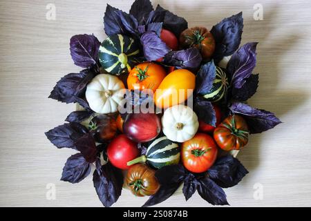 Tomates anciennes fraîchement récoltées, citrouilles et feuilles de basilic pourpres disposées sur une surface en bois, créant un affichage vibrant et coloré Banque D'Images