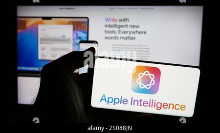 Dans cette illustration photo, une personne tient un smartphone avec le logo de la plate-forme d'IA Apple Intelligence devant le site Web. Banque D'Images