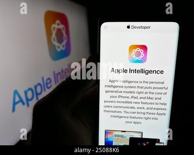 Dans cette illustration photo, une personne tient un smartphone avec le site Web de la plateforme d’IA Apple Intelligence devant le logo de l’entreprise. Banque D'Images