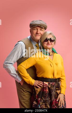 Portrait de l'homme mûr portant casquette en tweed et gilet se tient derrière la femme senior en blouse jaune et jupe à motifs, les deux souriant avec confiance contre Banque D'Images