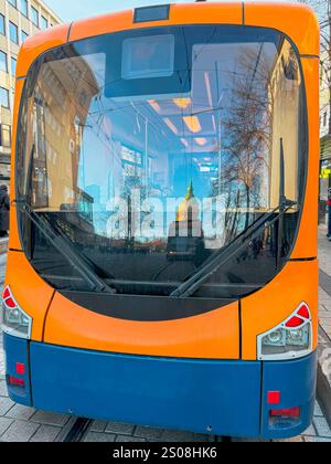 Tramway orange vif avec des reflets de la ville dans la fenêtre avant. Une scène urbaine moderne, les transports en commun Banque D'Images