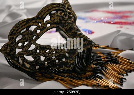 Élégant masque vénitien avec des perles couchées sur un tissu blanc avec des paillettes rouges, blanches et bleues, parfait pour célébrer le carnaval ou toute occasion spéciale. Banque D'Images