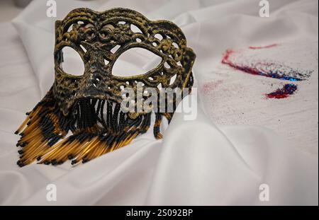 Élégant masque vénitien avec des perles couchées sur un tissu blanc avec des paillettes rouges, blanches et bleues, parfait pour célébrer le carnaval ou toute occasion spéciale. Banque D'Images