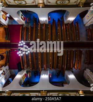 L'image capture une vue aérienne de l'intérieur d'une cathédrale, présentant des bancs en bois symétriques, un lustre central et des détails architecturaux ornés. Banque D'Images