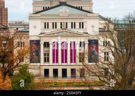 L'Opéra national letton de Riga présente une façade néoclassique avec de hautes colonnes et des sculptures. Des arbres d'automne entourent le bâtiment, ajoutant de la couleur. Banque D'Images