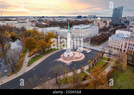 Vue aérienne de Riga, Lettonie, mettant en évidence le Monument de la liberté au milieu d'une place circulaire et d'arbres d'automne. Le paysage urbain présente une architecture diversifiée. Banque D'Images