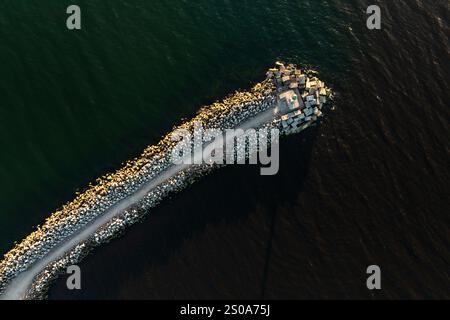 Une perspective aérienne d'une longue jetée avec de gros rochers et des blocs de béton à son extrémité, contrastant avec les eaux profondes qui l'entourent. Banque D'Images