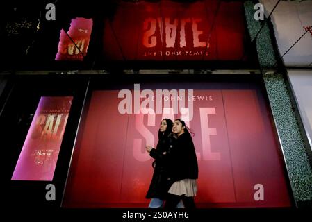 Londres, Grande-Bretagne. 26 décembre 2024. Deux femmes passent devant un panneau de vente à l'extérieur d'un magasin pendant les soldes de Boxing Day à Londres, Grande-Bretagne, le 26 décembre 2024. Crédit : Li Ying/Xinhua/Alamy Live News Banque D'Images