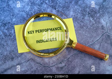 Concept commercial et financier. Mots KPI (Key performance Indicator) écrits à l'aide d'une loupe, vue de dessus sur papier jaune. Banque D'Images