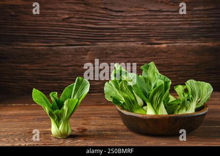 Une collection de bok choy vibrant dans un bol en bois rustique sur une table de cuisine en bois, avec un bok choy plus petit à côté, soulignant leur gree frais Banque D'Images