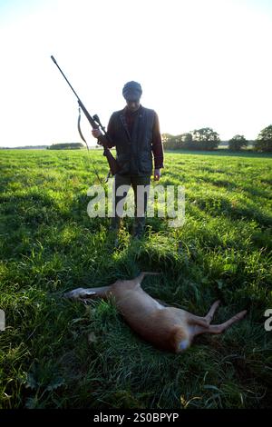 Un chasseur se tient debout sur sa mort dans un champ herbeux, lors d'un voyage de chasse au cerf en Zélande, au Danemark. Banque D'Images