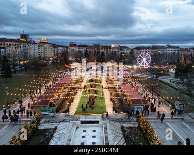 Une vue aérienne captivante du marché de Noël de Sofia au crépuscule, près de NDK, avec des lumières vibrantes, des stands festifs, une grande roue, et les fêtes de fin d'année. Banque D'Images