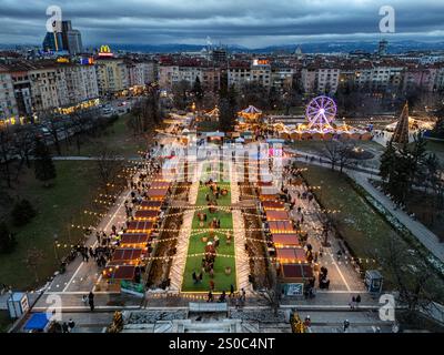 Une vue aérienne captivante du marché de Noël de Sofia au crépuscule, près de NDK, avec des lumières vibrantes, des stands festifs, une grande roue, et les fêtes de fin d'année. Banque D'Images