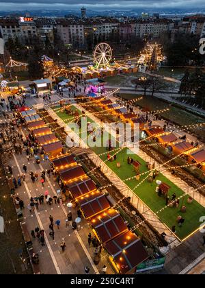 Une vue aérienne captivante du marché de Noël de Sofia au crépuscule, près de NDK, avec des lumières vibrantes, des stands festifs, une grande roue, et les fêtes de fin d'année. Banque D'Images
