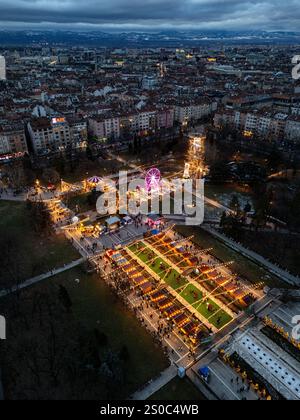 Une vue aérienne captivante du marché de Noël de Sofia au crépuscule, près de NDK, avec des lumières vibrantes, des stands festifs, une grande roue, et les fêtes de fin d'année. Banque D'Images