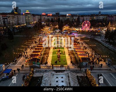 Une vue aérienne captivante du marché de Noël de Sofia au crépuscule, près de NDK, avec des lumières vibrantes, des stands festifs, une grande roue, et les fêtes de fin d'année. Banque D'Images