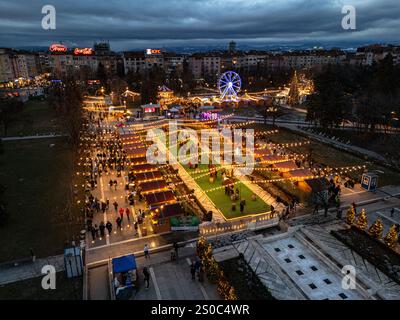 Une vue aérienne captivante du marché de Noël de Sofia au crépuscule, près de NDK, avec des lumières vibrantes, des stands festifs, une grande roue, et les fêtes de fin d'année. Banque D'Images