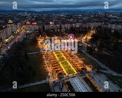 Une vue aérienne captivante du marché de Noël de Sofia au crépuscule, près de NDK, avec des lumières vibrantes, des stands festifs, une grande roue, et les fêtes de fin d'année. Banque D'Images