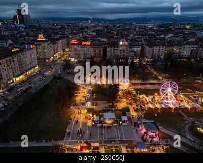Une vue aérienne captivante du marché de Noël de Sofia au crépuscule, près de NDK, avec des lumières vibrantes, des stands festifs, une grande roue, et les fêtes de fin d'année. Banque D'Images
