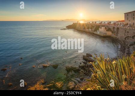 Piombino, vue sur la Piazza Bovio et le phare au coucher du soleil, île d'Elbe en arrière-plan et un peu de végétation au premier plan. Maremme, province de Banque D'Images